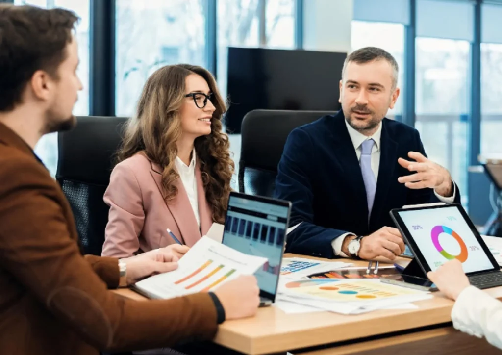 Marketing team reviewing charts and analytics on laptops and tablets during a strategy meeting, discussing performance data and campaign optimization.
