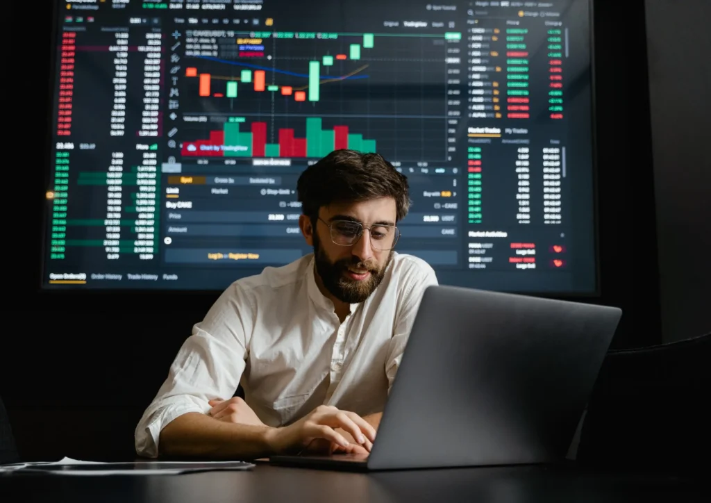 Person analyzing performance charts on a laptop with a large data dashboard in the background, representing real-time optimization for Meta’s AI systems.