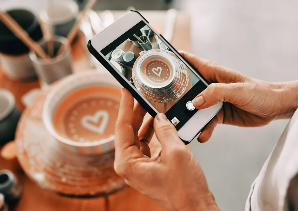 Hands photographing handmade pottery with a smartphone, representing UGC-style creative and authentic visual content used by Meta’s AI for ad targeting.