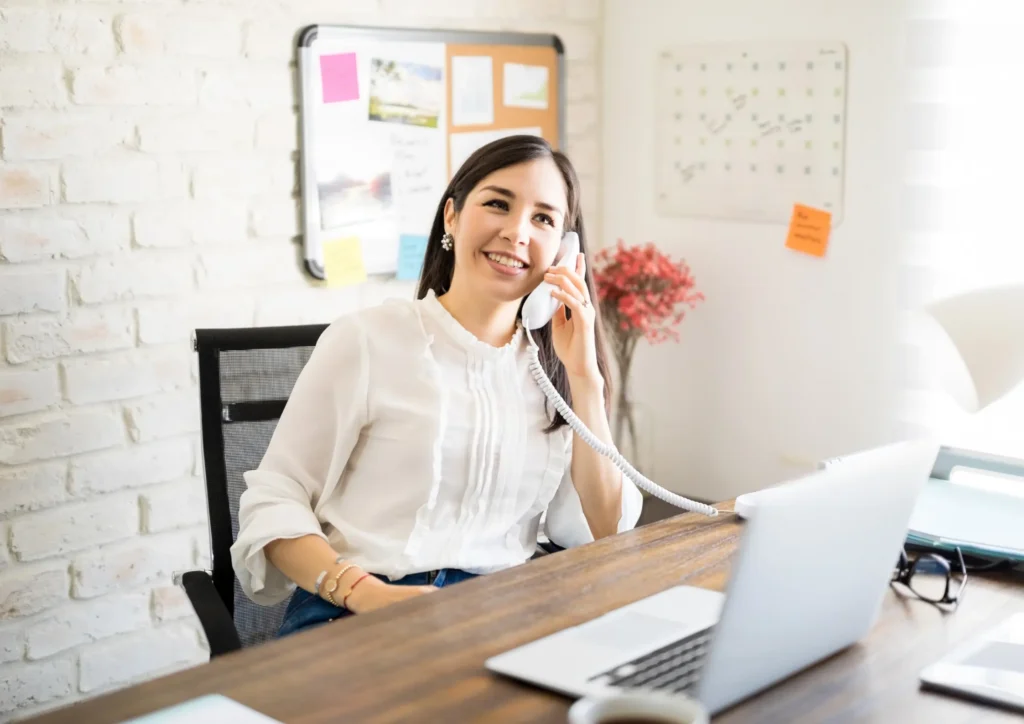 Person smiling while talking on a phone at a desk, representing outbound lead generation through direct outreach.
