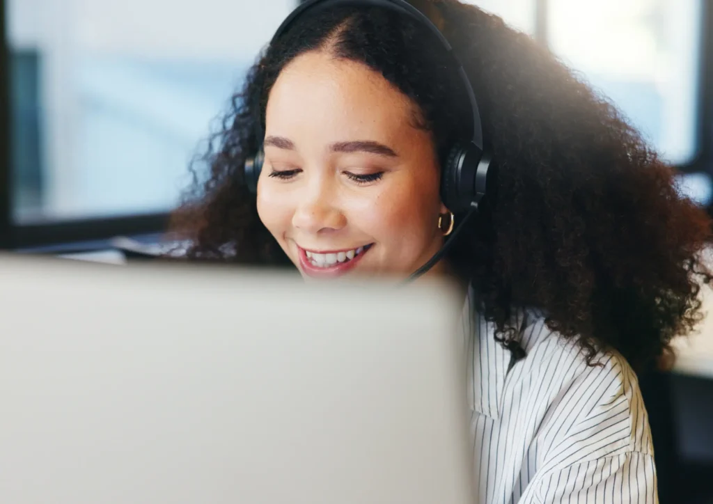 Person wearing a headset smiling while working on a computer, representing outbound lead generation through calls and direct outreach.