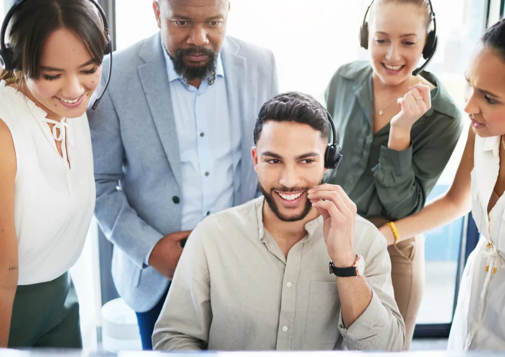 Team gathered around a coworker wearing a headset, demonstrating outbound lead generation and collaborative outreach.